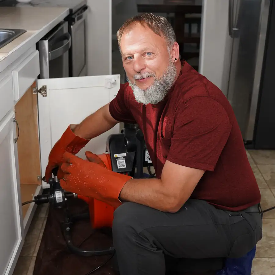 Plumber with tools kneeling under a sink